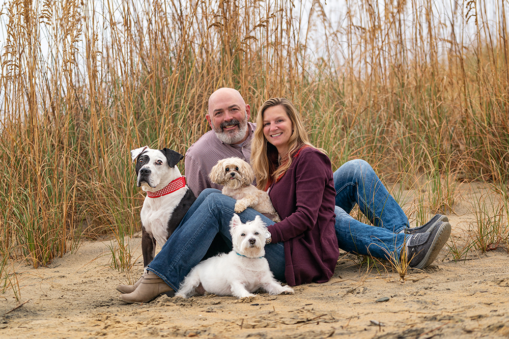 Three dogs and their family pose on the dunes in Norfolk Virginia